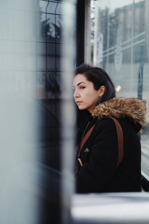 a woman in a black coat sitting at a window looking outside