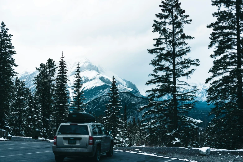 car traveling on snow covered road with trees and mountain in background