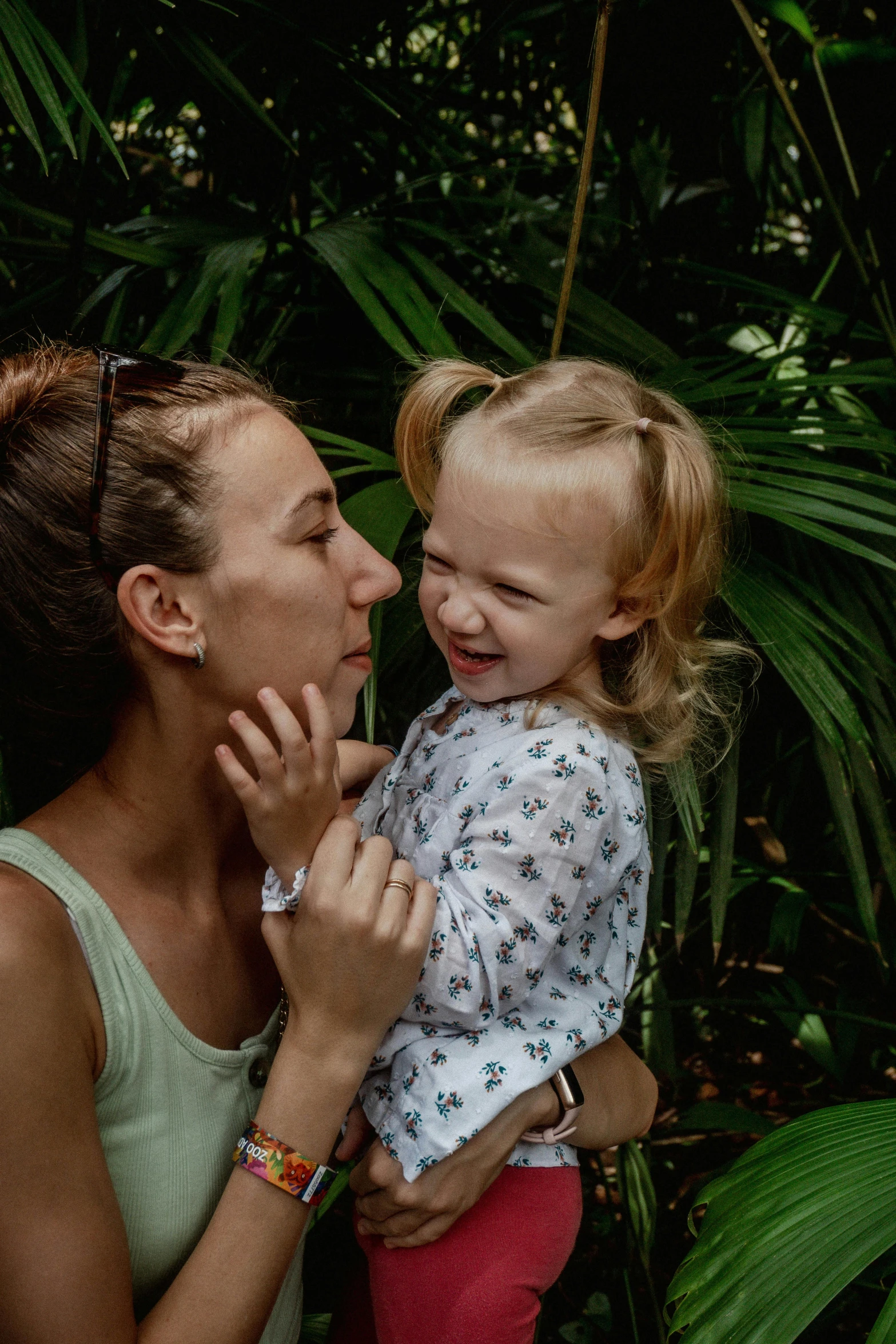 woman holding and touching her laughing toddler while outside