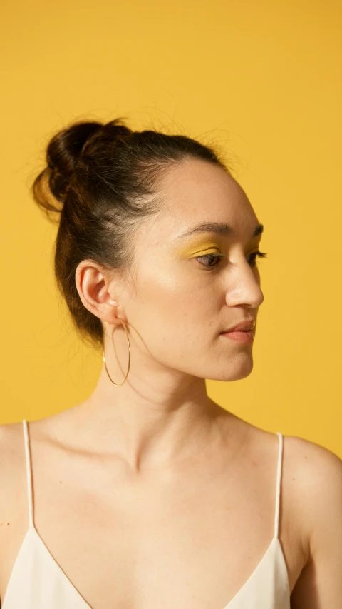a woman with a messy bun and eye makeup has yellow eyeshadow