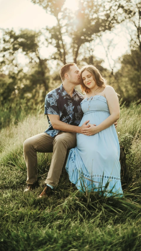 a pregnant couple sit in tall grass at sunset