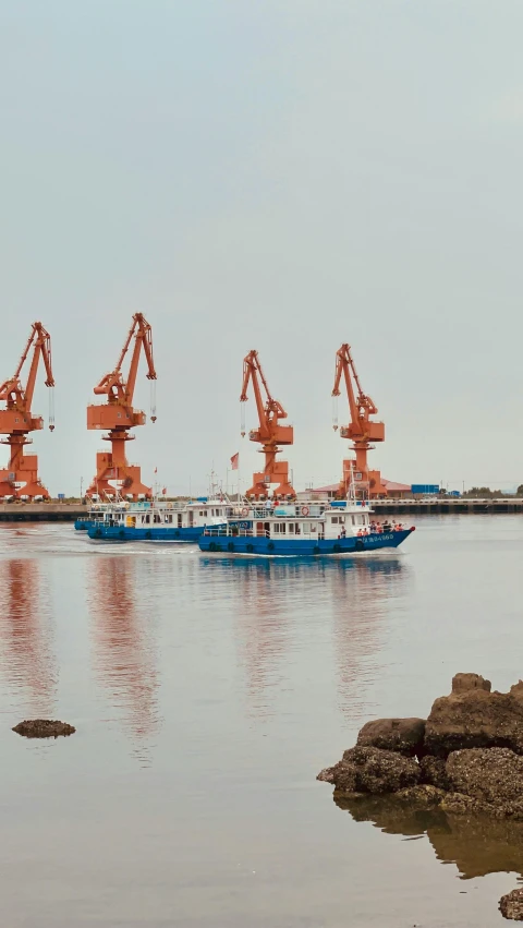 blue and white boat in ocean next to orange cranes