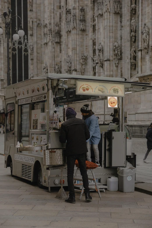 people are eating from food truck, near large brick building