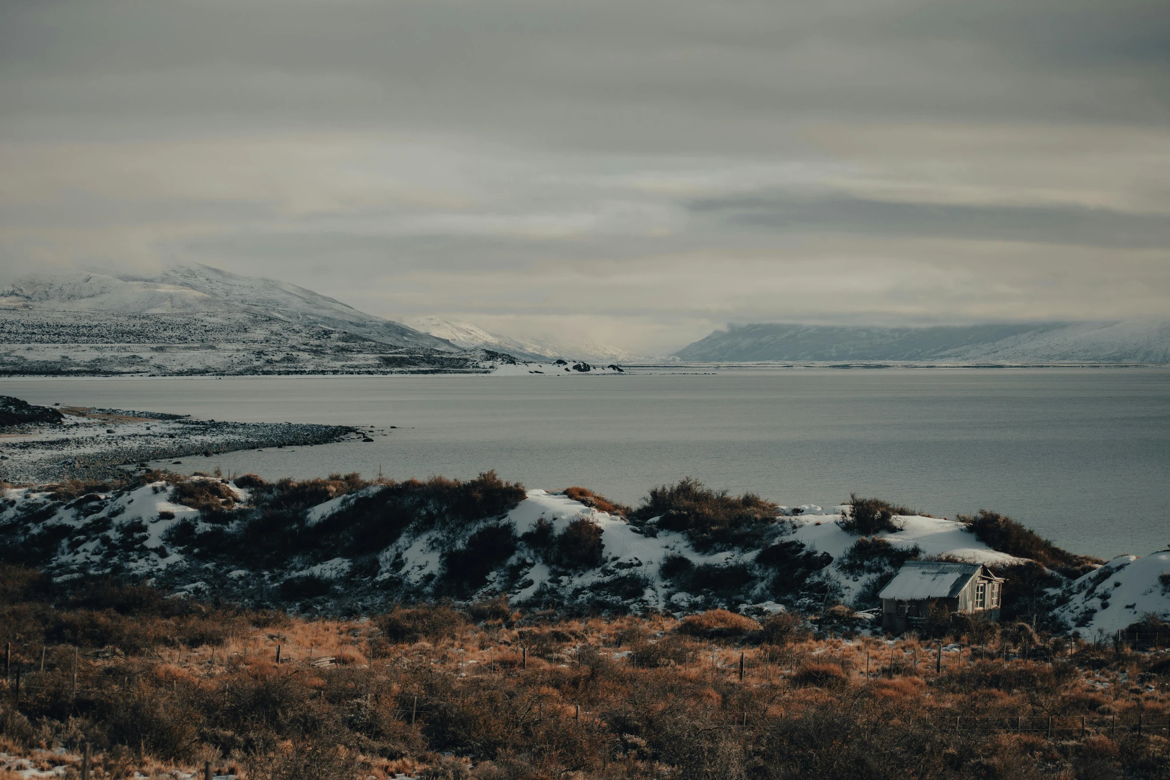 landscape pograph of a snowy mountain lake with brown bushes