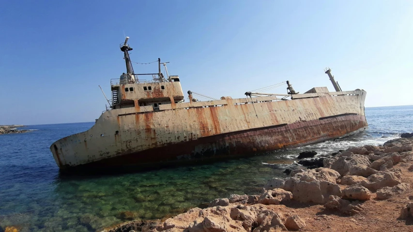 a rusted old ship docked in the ocean on a rock shore