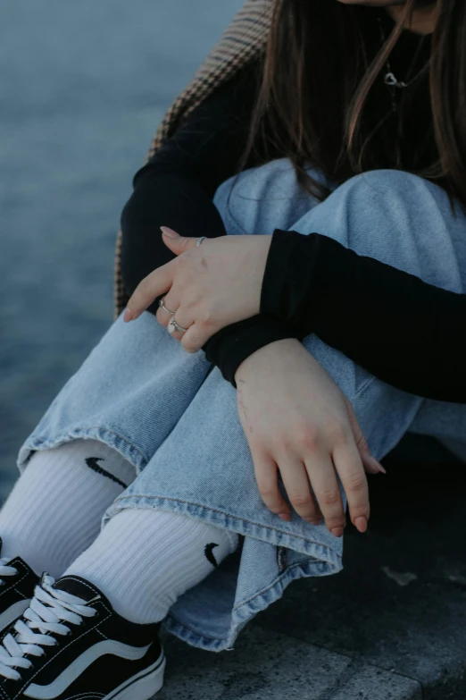 a woman in black shirt and jeans sitting by water