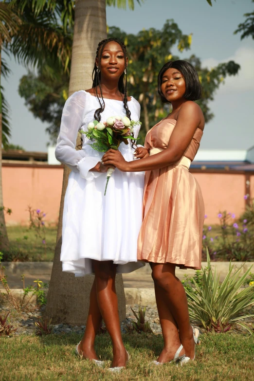 two women in dresses standing together near trees