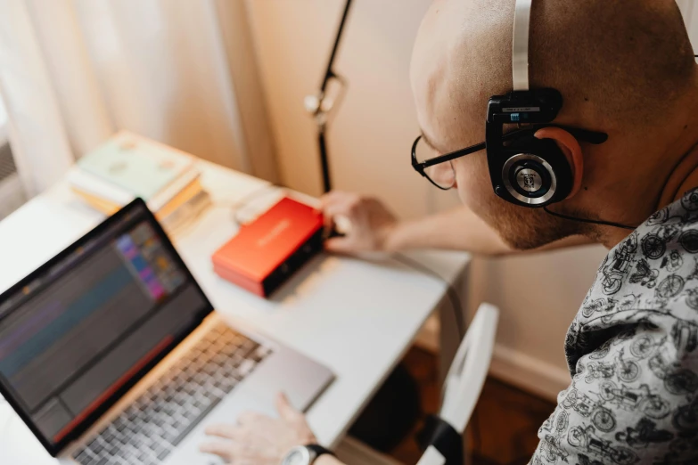 the head of an adult with headphones and ear phones near a laptop