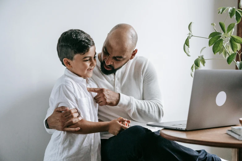 a man helping a boy fix his tie in front of a laptop computer