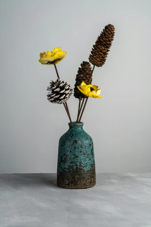 an artistic vase with two pine cones and three yellow flowers in it