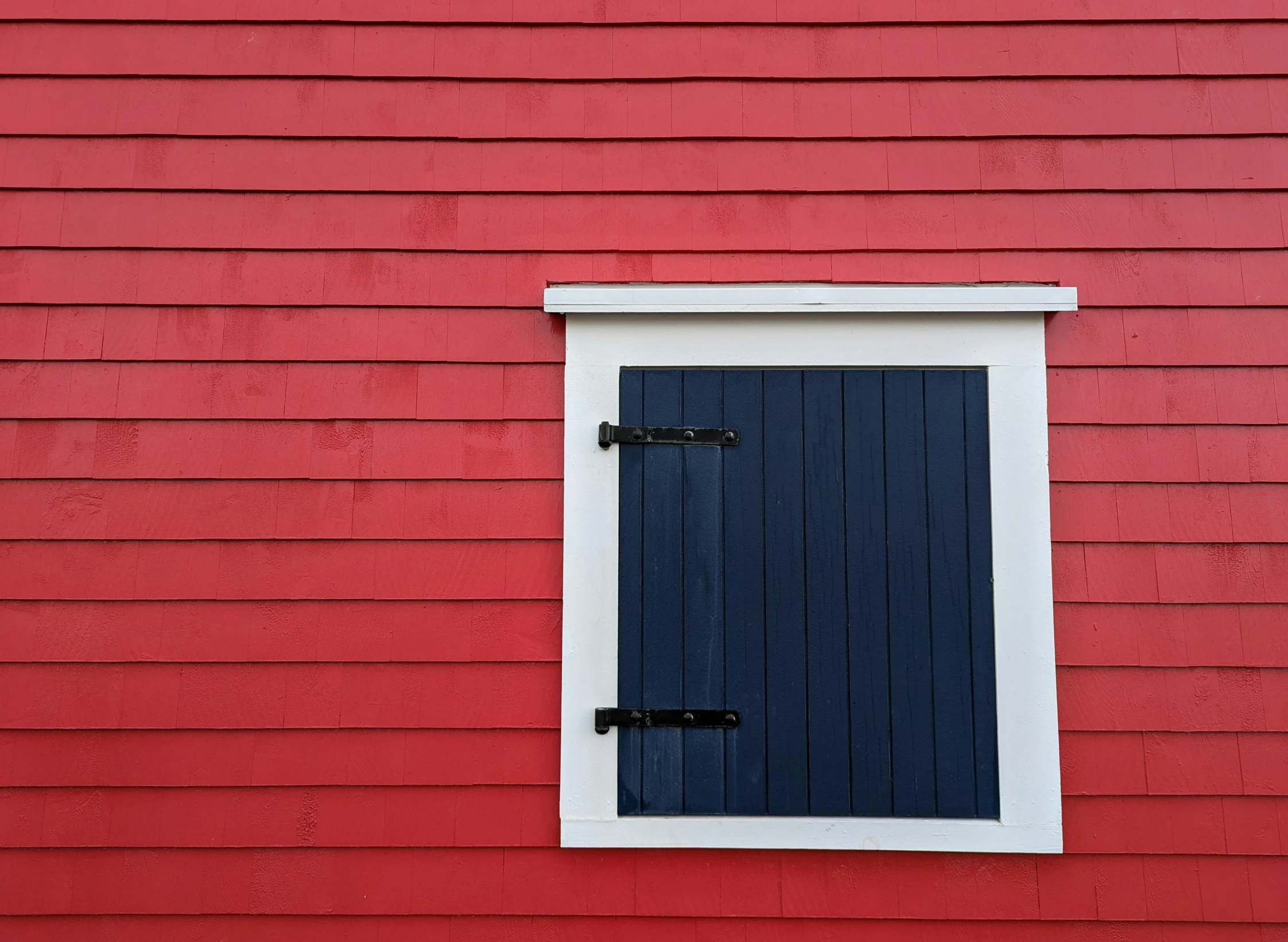 a red building with a white window and dark wooden shutters