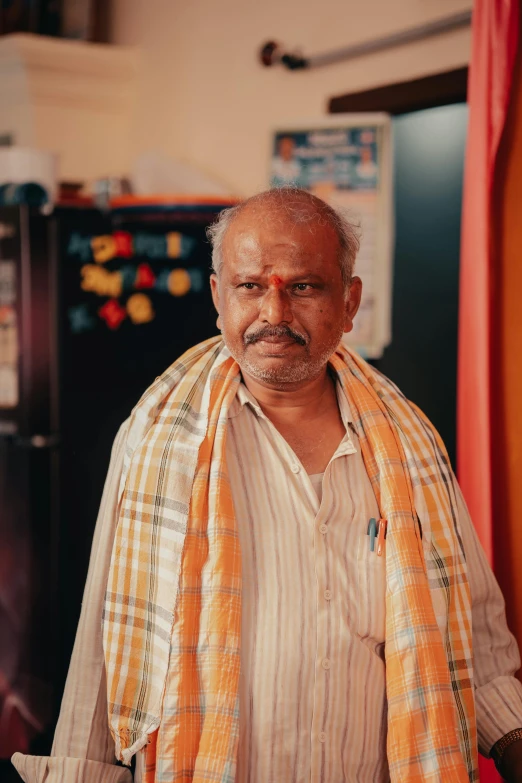 an old man wearing a scarring next to a fridge