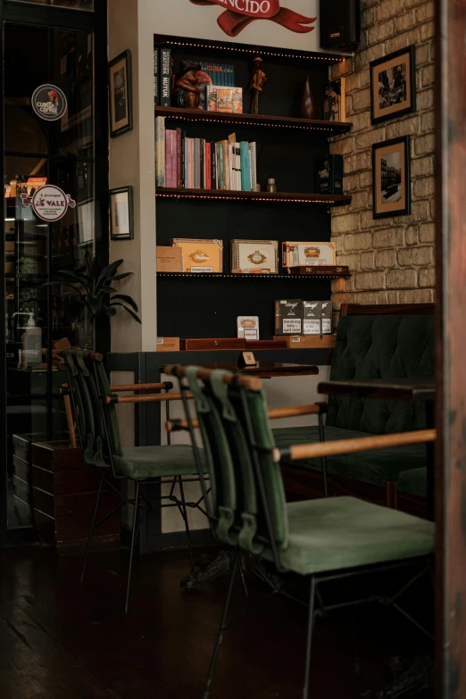 a room with two tables and chairs, some books on a shelf, a brick wall and many framed pictures