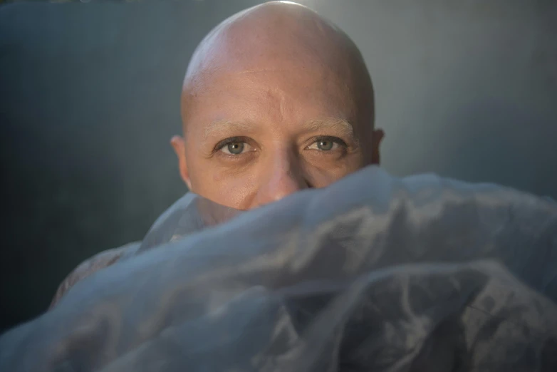 a balding man peeks his head out from a large sheet