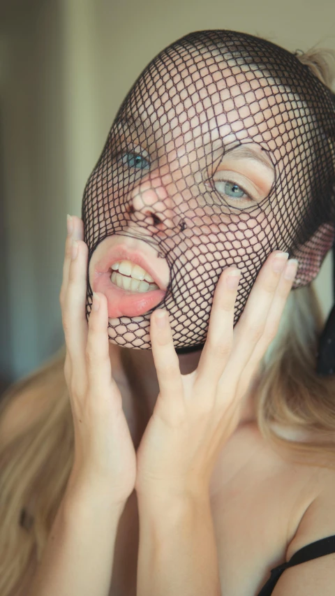 a woman holding her face up with fishnet covering her face