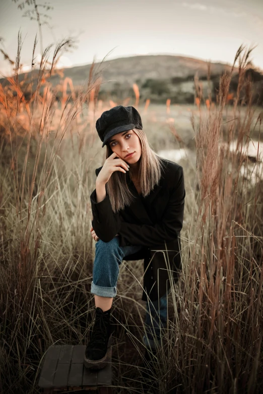 a girl with her hands on her face sitting in the middle of a tall grass field