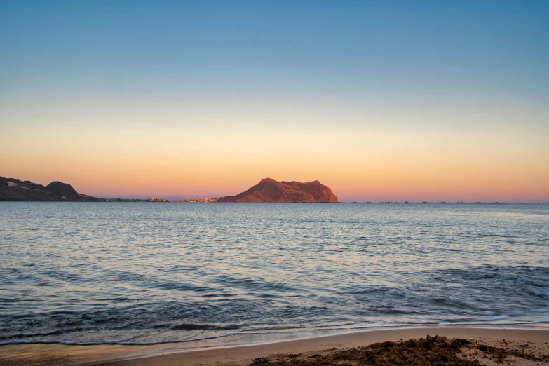 an empty beach next to a mountain at sunset