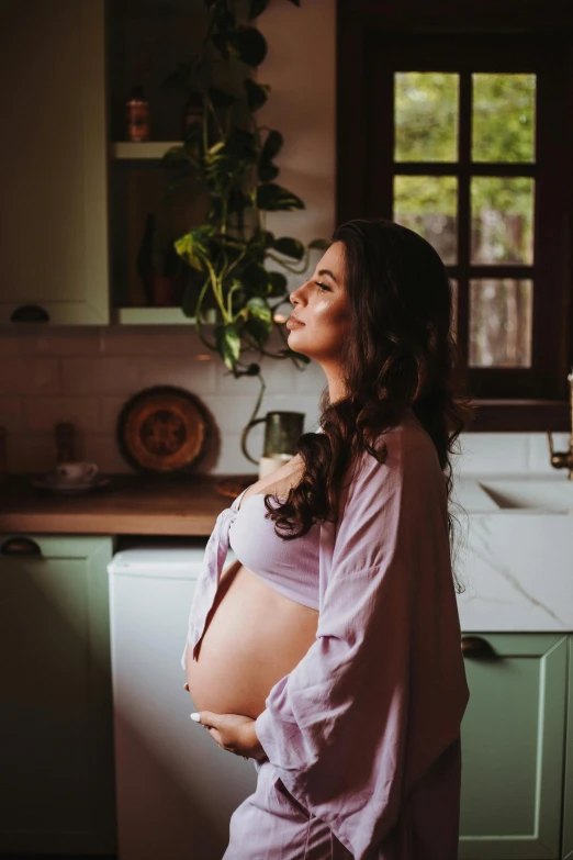 a pregnant woman in a pink shirt stands on a kitchen counter