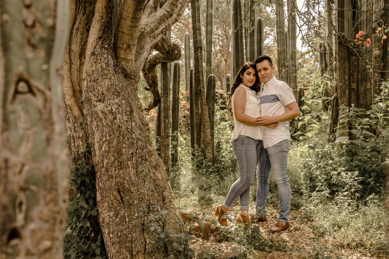 a couple cuddling next to a grove of trees