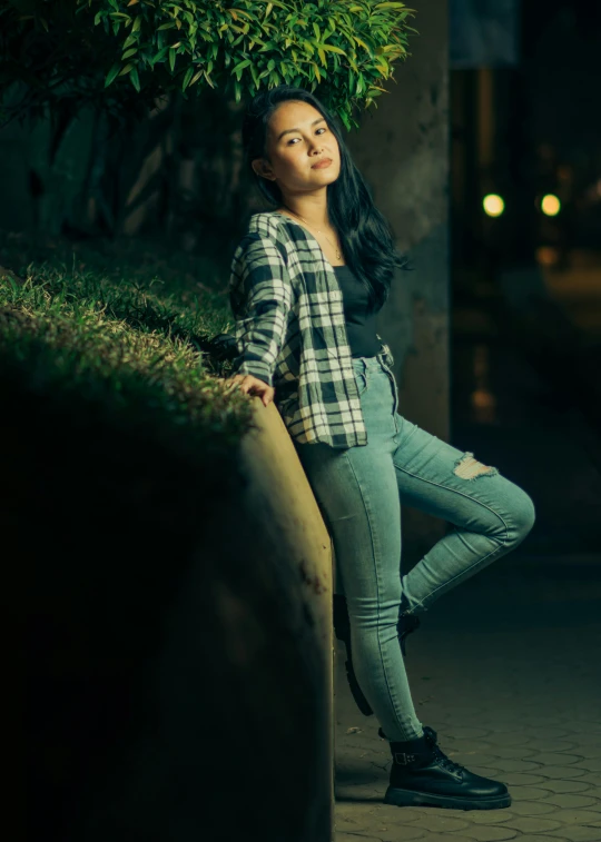 a woman leaning against a wooden pole in front of a bush