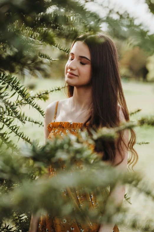 a woman wearing a yellow dress stands next to a tree