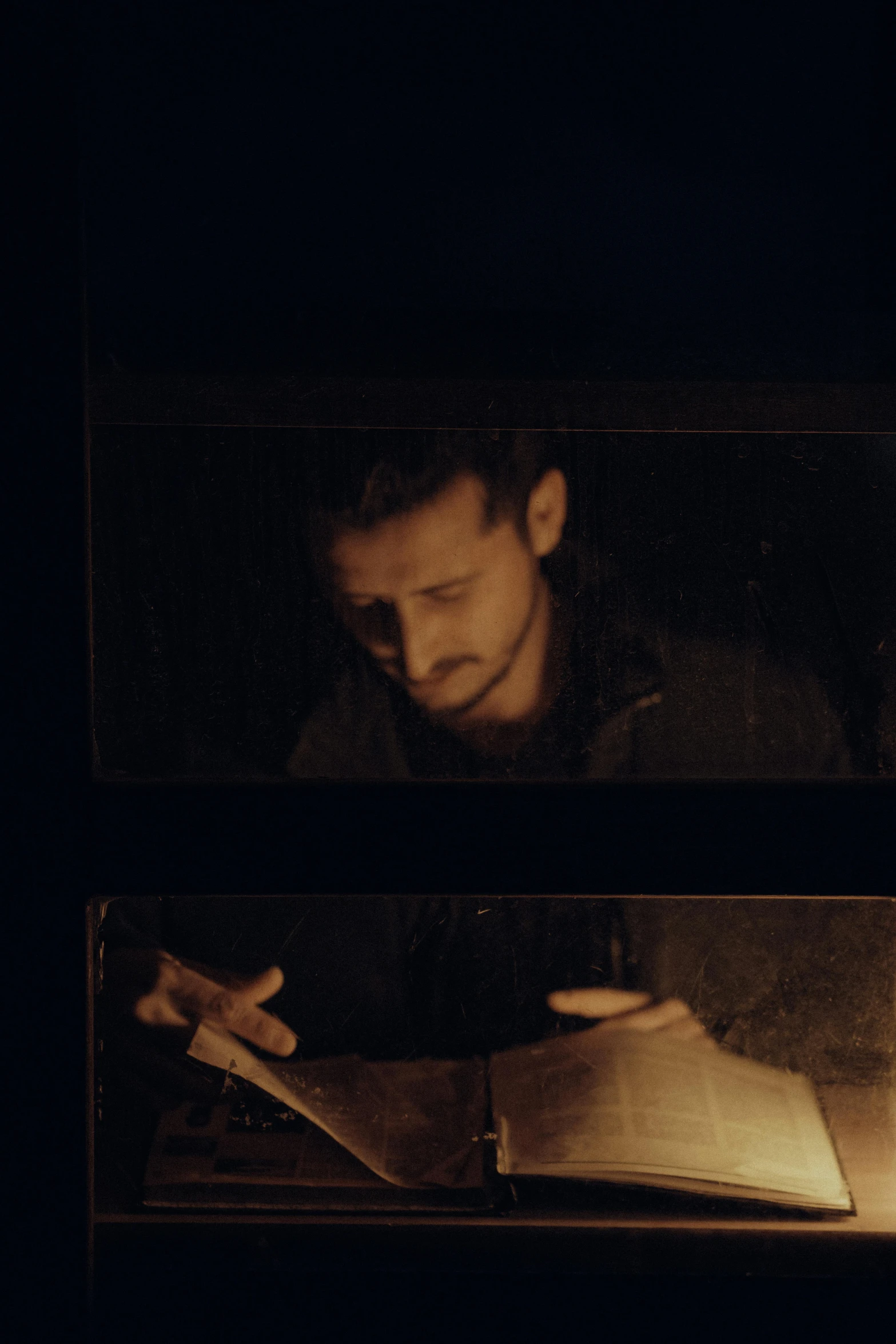 man sitting in dark room looking at open book with burning papers