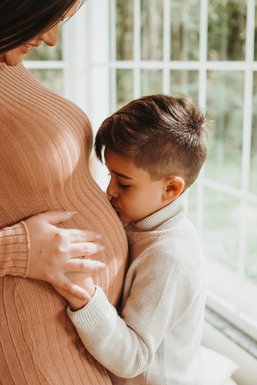 a pregnant woman in a turtle neck sweater holds a child's stomach