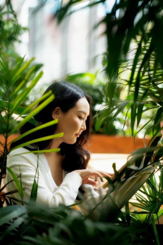 a woman looks down on her cellphone while standing in front of large plants
