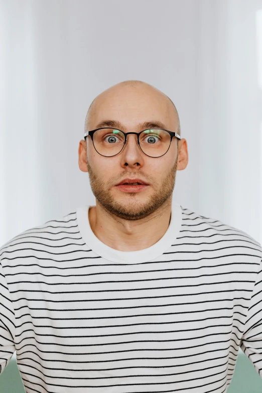 a bald man with glasses standing in front of a white wall