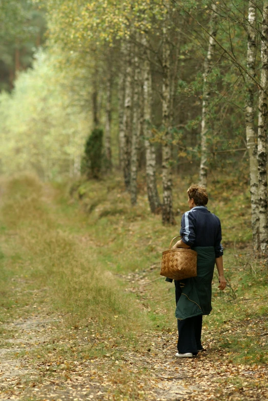 a man with a brown basket walking down a leafy dirt road