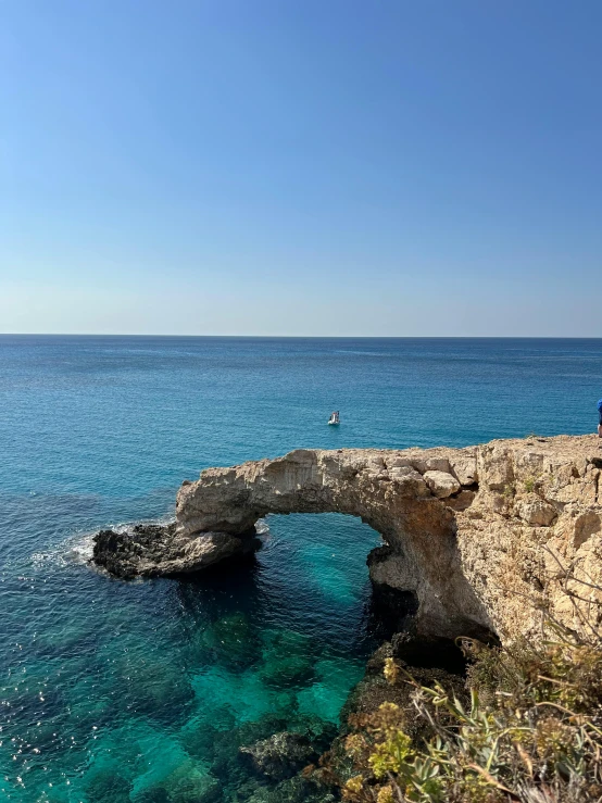 a man is fishing at an ocean with a rock bridge