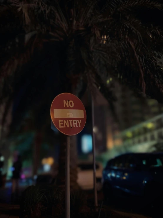 a no entry sign next to a car parked along a street at night