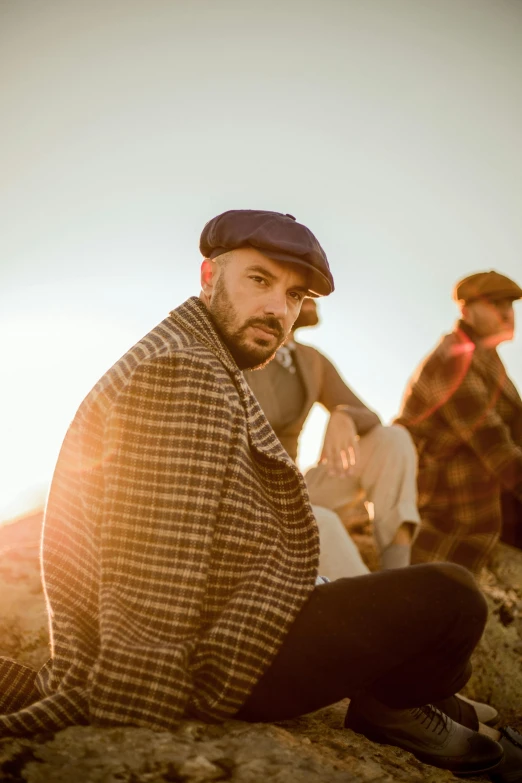 two men sitting on a hill while one in the process of posing for a po