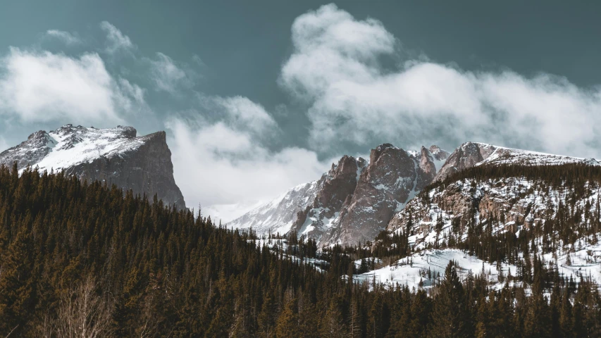 the clouds are rolling over the mountains covered with snow