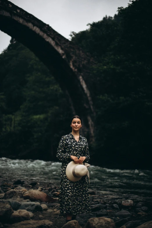 a woman standing on a river bank holding her hat