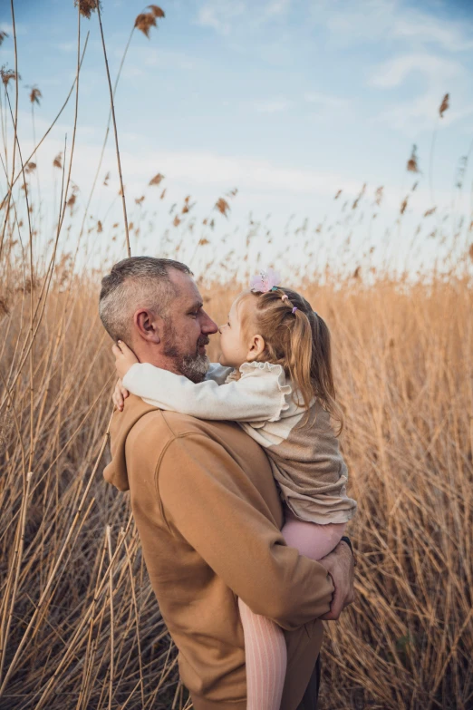 a man is holding his small daughter while standing in a tall grass field