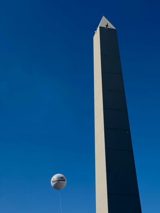 two balloons fly beneath the washington monument against a blue sky