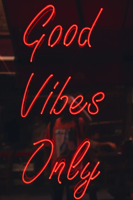 a person standing under a red sign saying good vibes only