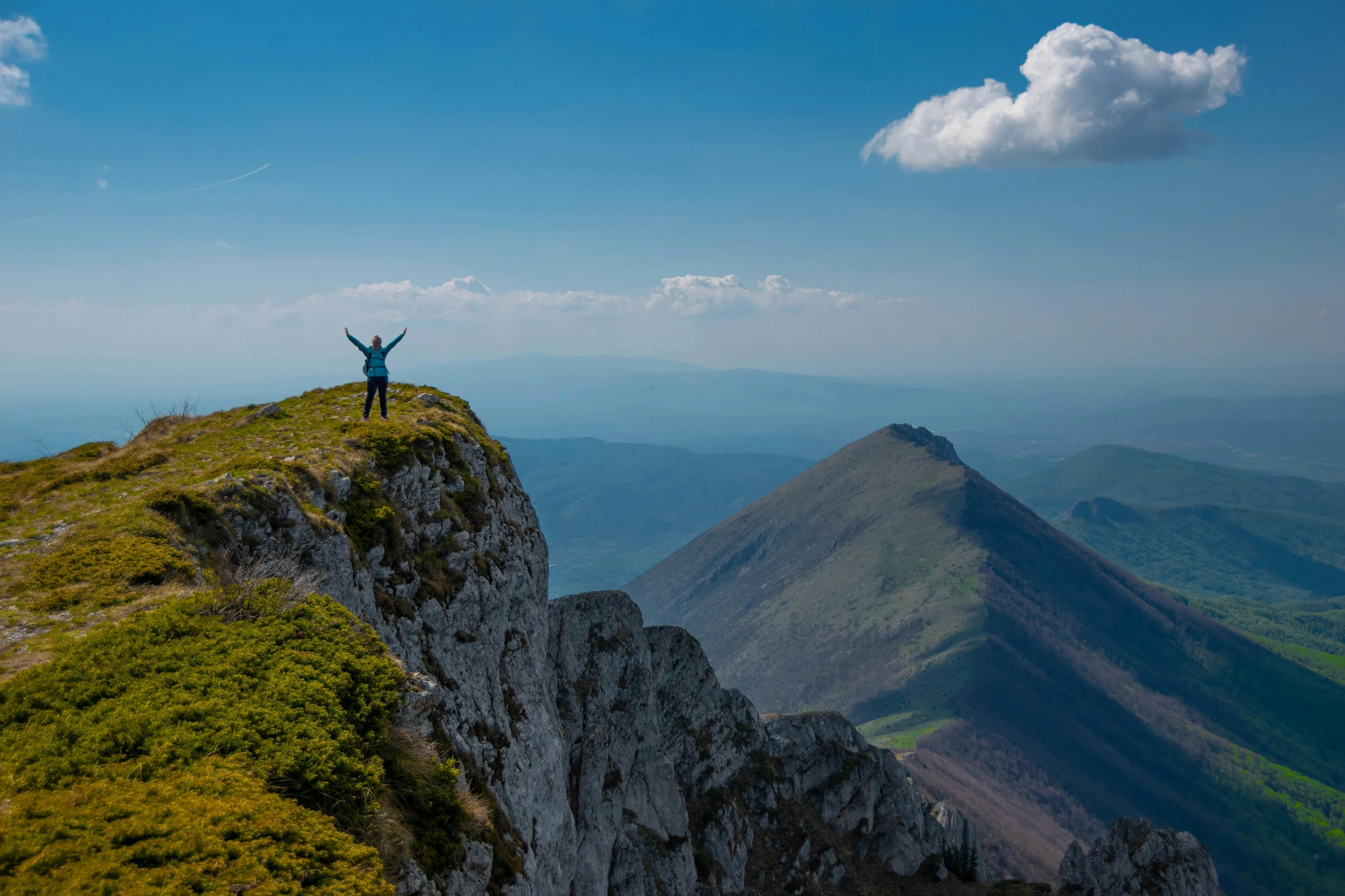 a man standing on top of a mountain above a lush green hillside