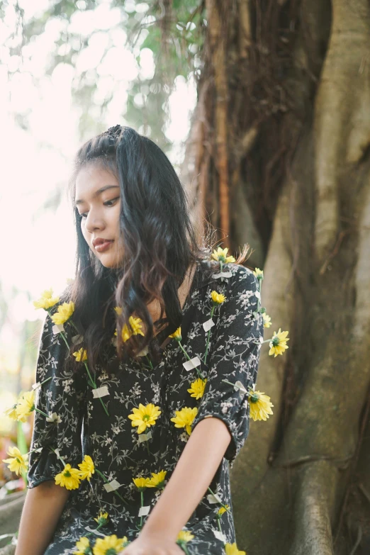 a girl with flowers in a dress sits on a rock looking down at her phone