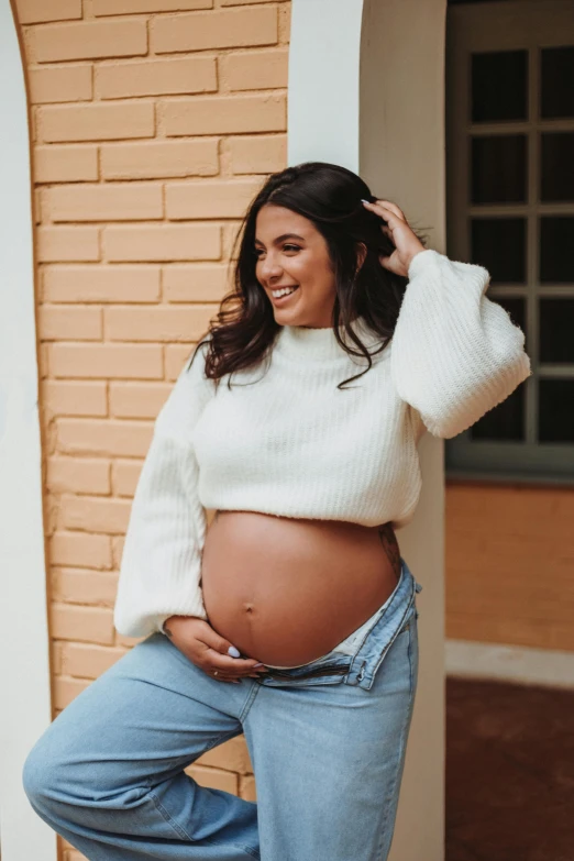 a pregnant woman poses in jeans and a sweater