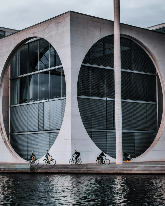 people are biking near an architectural building next to water