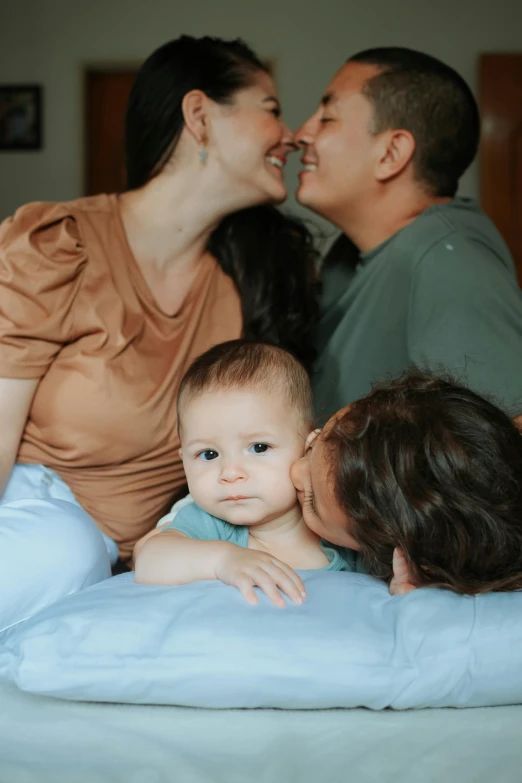 a couple kissing a baby on top of a bed