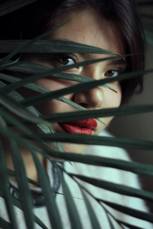 a woman with red lipstick behind a tropical plant