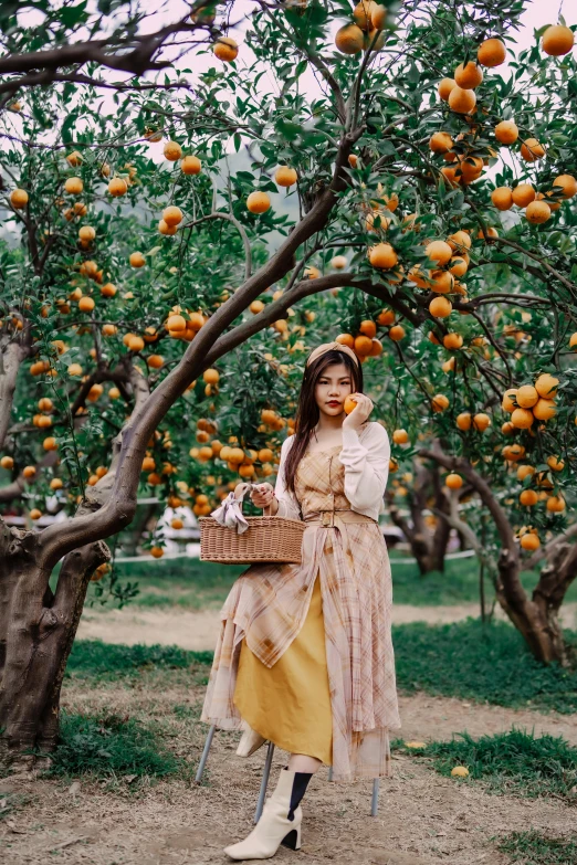 woman standing under an orange tree with one hand on her shoulder