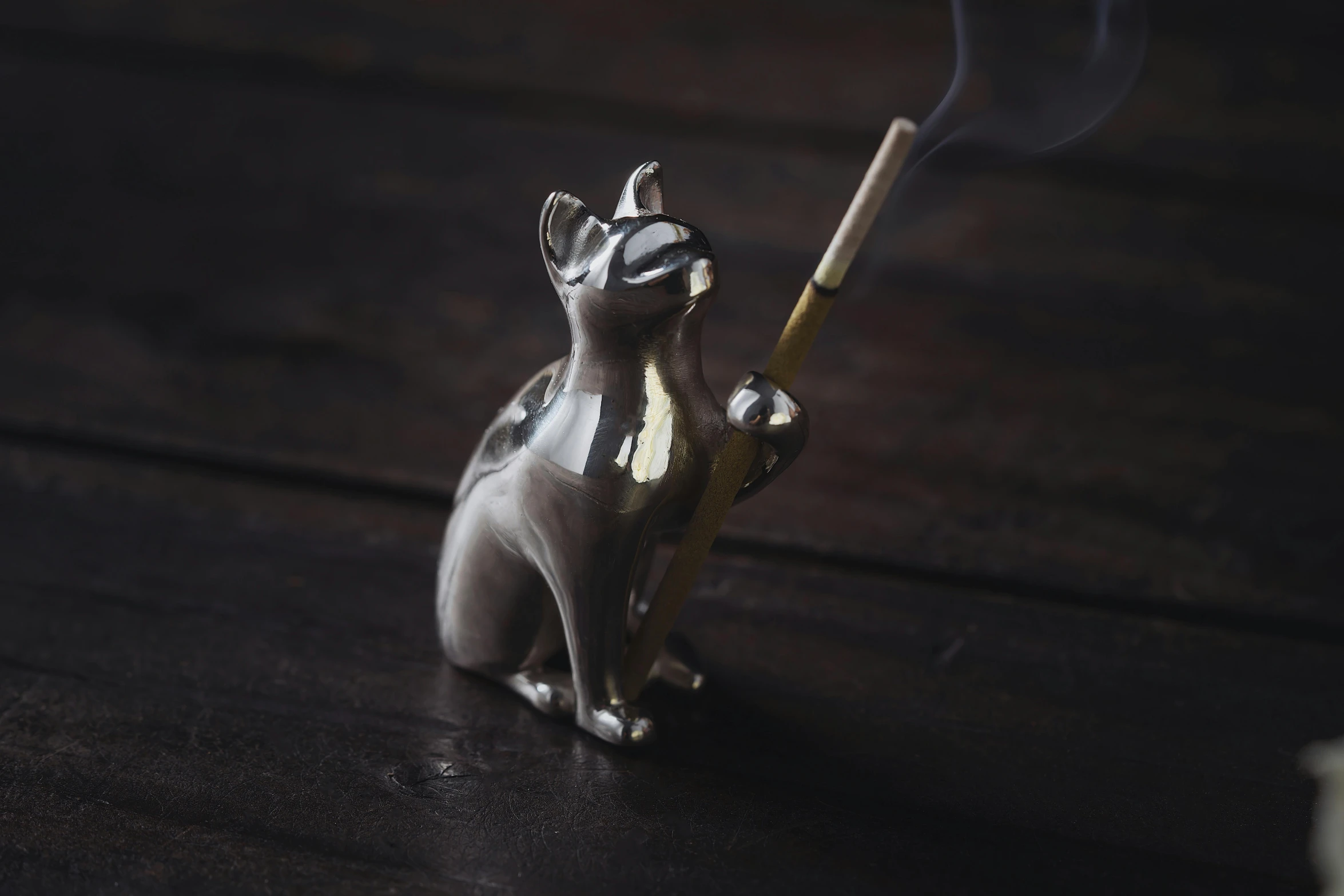 a little metal statue of a cat holding a incense stick