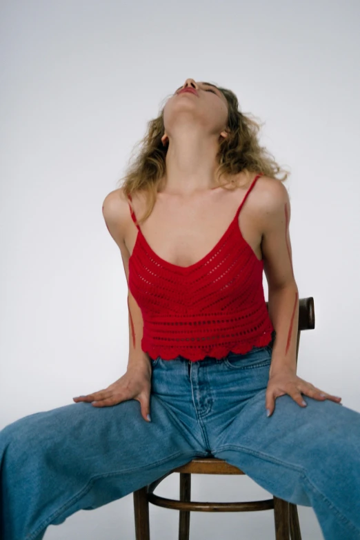 a woman in a red top, jeans and heels sits on a stool