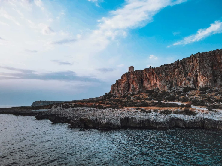 a cliff face with some water and rocks below