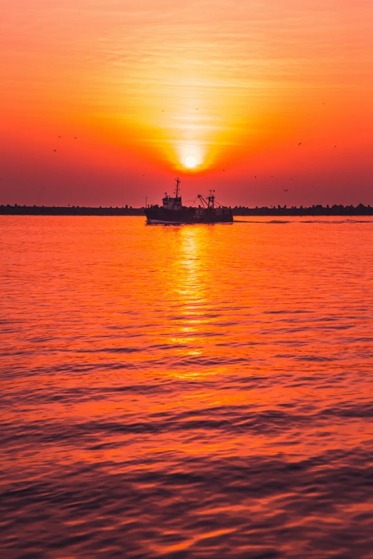 the sun setting over the water as a boat sails by