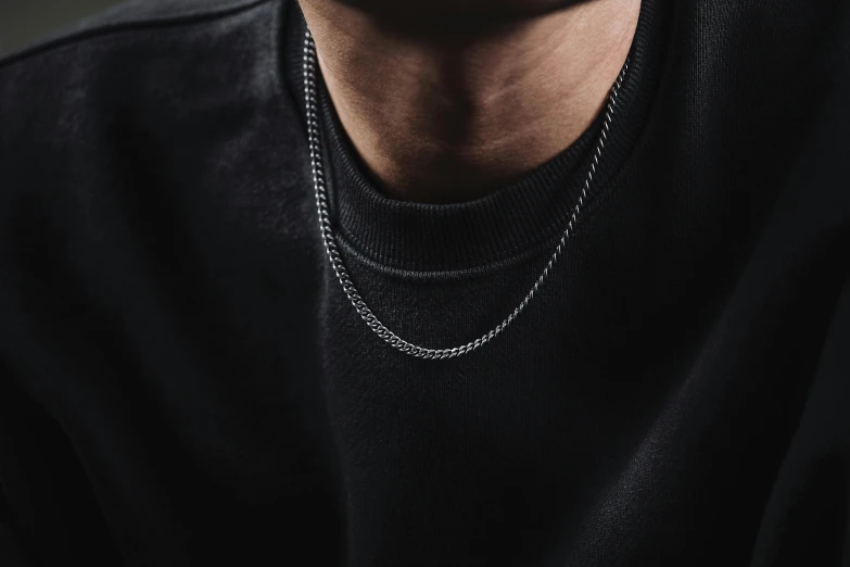 a young man is wearing a black sweater and white necklace